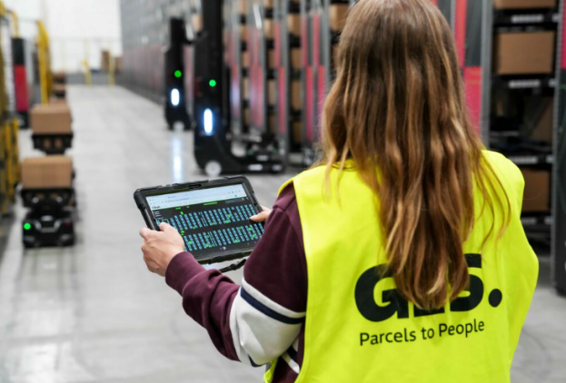 Operaria de GLS en almacén gestionando envíos con tablet digital en centro logístico automatizado.