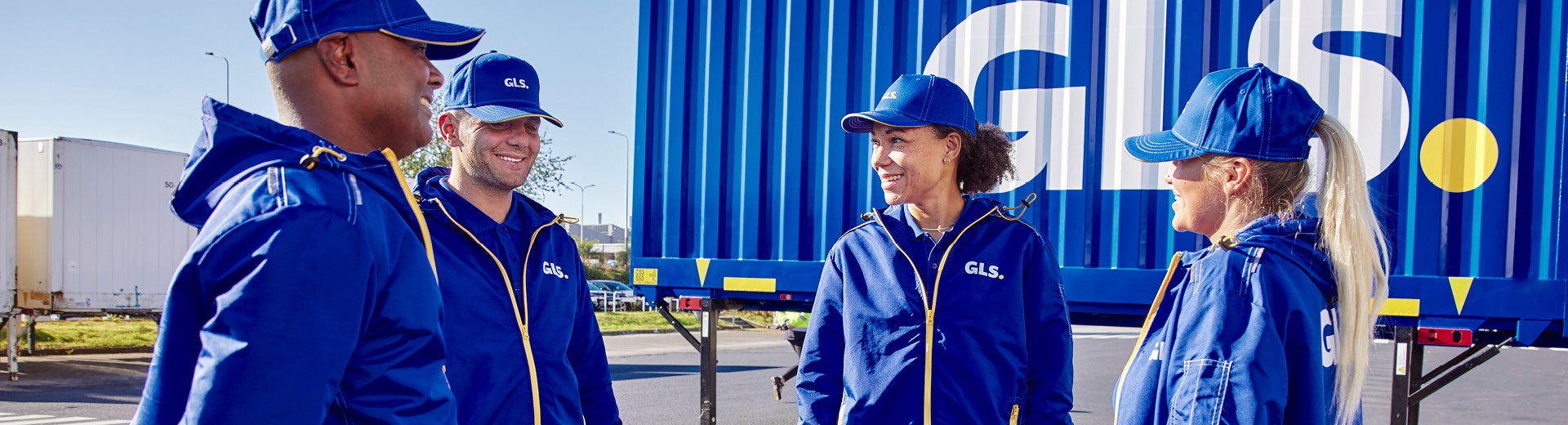 Employés GLS en tenue professionnelle sur site logistique, devant un conteneur de transport, illustrant les services de livraison de colis et la logistique du dernier kilomètre.