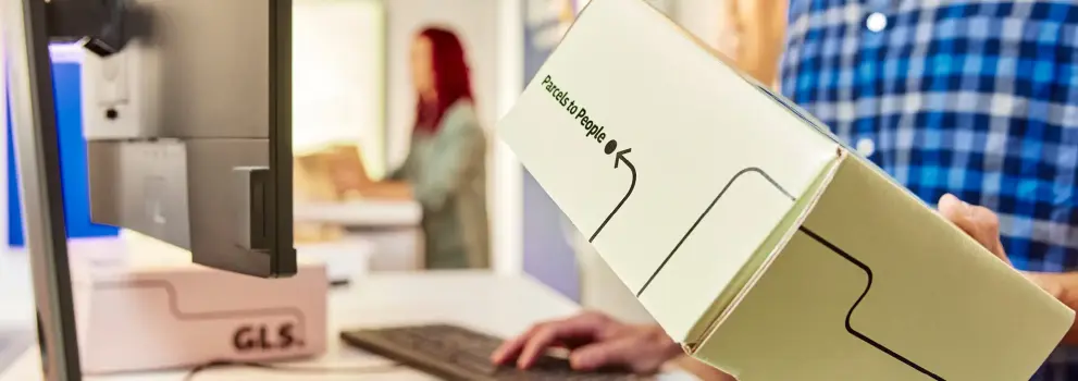 Close-up of a customer handing over a GLS parcel at a shipping counter, highlighting a shipping solution for professionals.