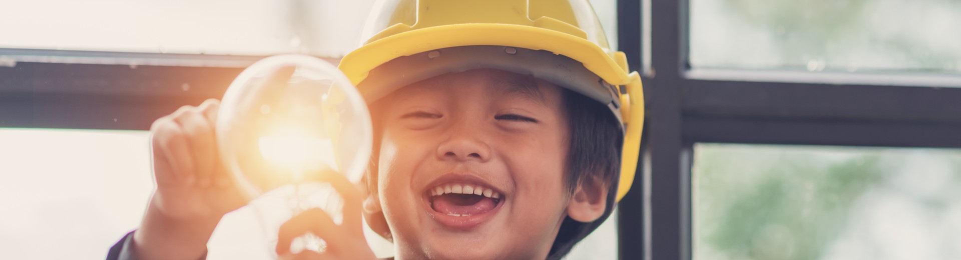 A child wearing a safety helmet holds a light bulb.